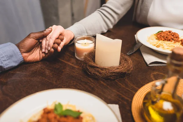 Vista recortada del hombre afroamericano cogido de la mano de un amigo y rezando durante la cena - foto de stock