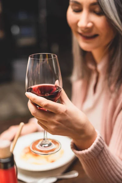 Selective focus of smiling asian woman holding wine glass during dinner — Stock Photo