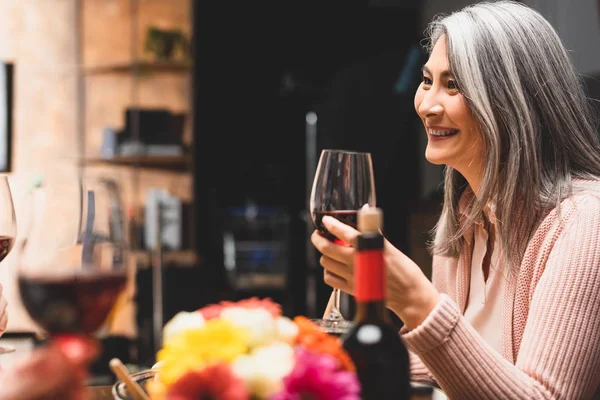 Enfoque selectivo de sonriente mujer asiática sosteniendo copa de vino durante la cena - foto de stock