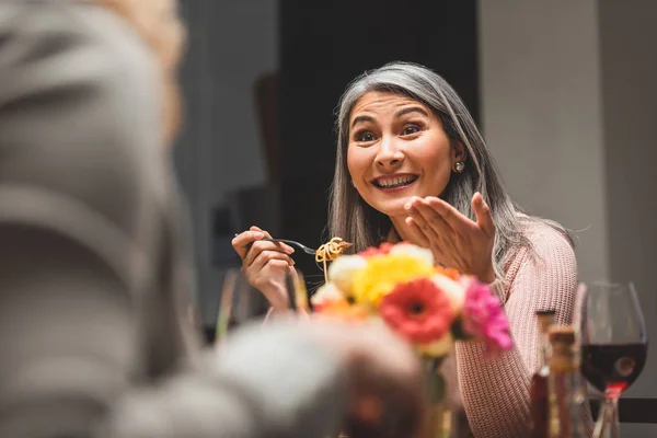 Selective focus of smiling asian woman eating pasta and talking with friend during dinner — Stock Photo