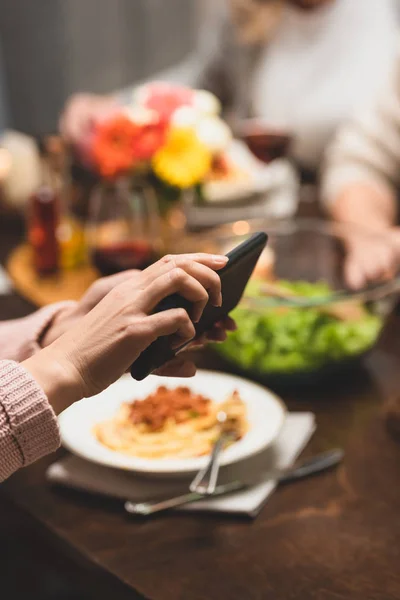 Cropped view of woman holding smartphone during dinner — Stock Photo