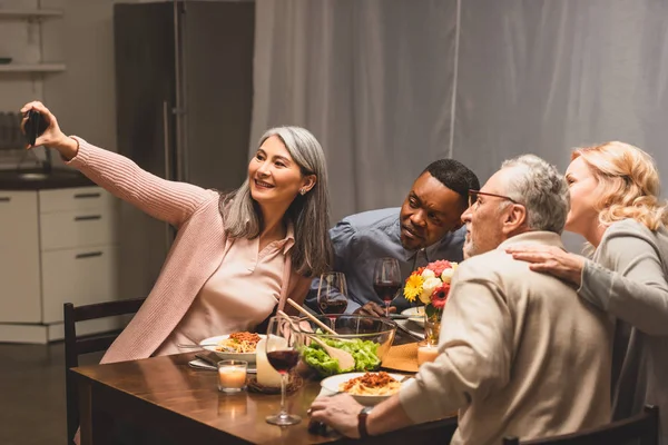 Lächelnde multikulturelle Freunde, die beim Abendessen ein Selfie mit dem Smartphone machen — Stockfoto