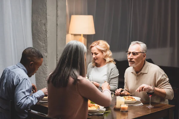 Enfoque selectivo de sonreír hombre y mujer hablando con amigos multiculturales y comiendo durante la cena — Stock Photo