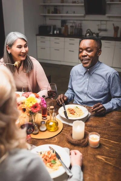 Enfoque selectivo de hombre y mujer multicultural hablando con un amigo durante la cena - foto de stock