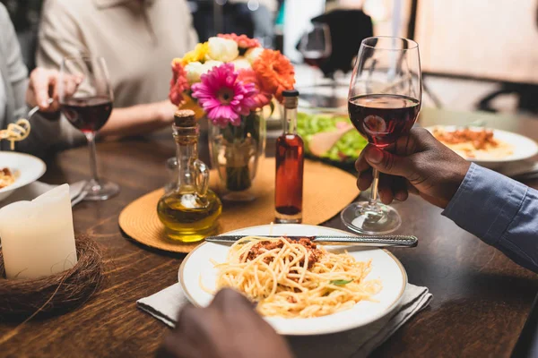 Vista cortada do homem americano africano segurando copo de vinho durante o jantar — Fotografia de Stock