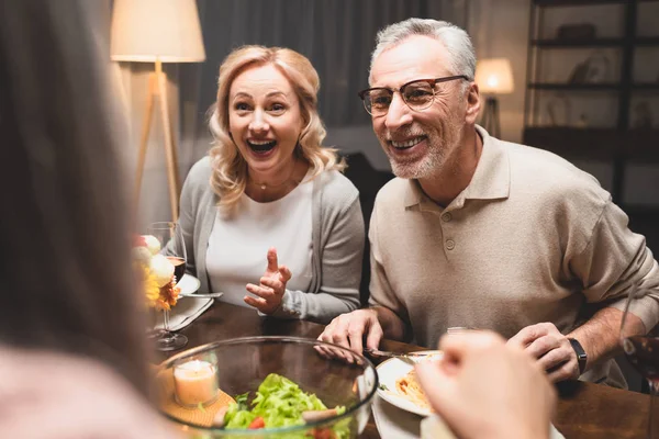 Вибірковий фокус усміхненого чоловіка і жінки, що розмовляє з другом під час вечері — стокове фото
