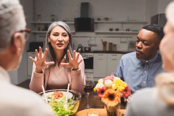 Foco seletivo de homem multicultural e mulher conversando com amigos durante o jantar — Fotografia de Stock