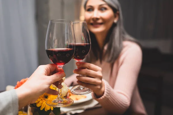 Recortado vista de la mujer tintineo con su sonriente asiático amigo durante la cena - foto de stock