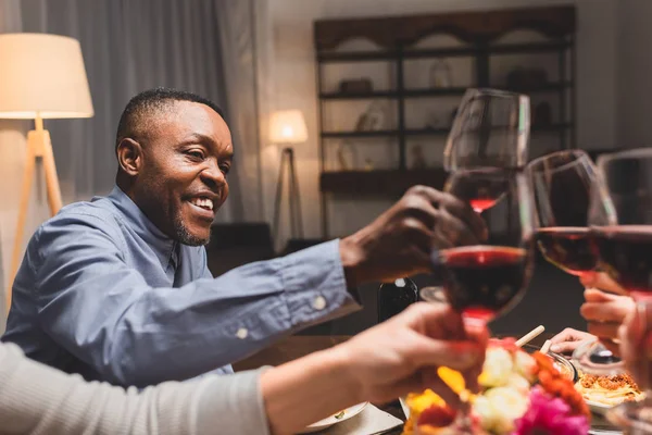 Vista cortada de amigos clinking com o homem americano africano durante o jantar — Fotografia de Stock