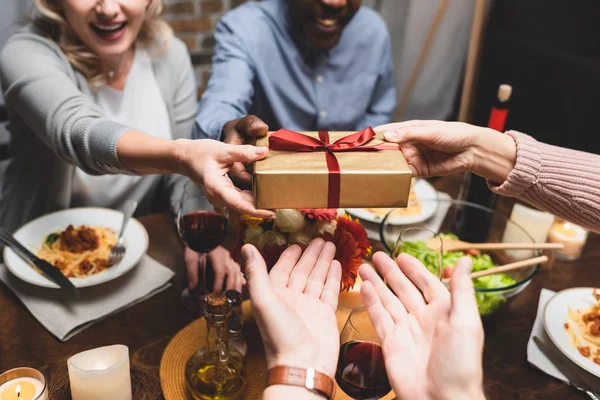 Vista recortada de hombre y mujer multicultural dando regalo a los amigos durante la cena - foto de stock