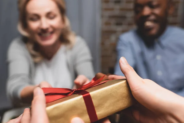 Cropped view of woman giving present to multicultural friends during dinner — Stock Photo