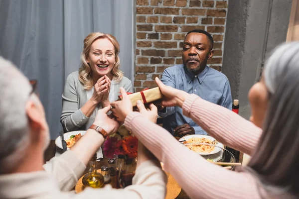 Abgeschnittene Ansicht von Frau und Mann, die lächelnden multikulturellen Freunden beim Abendessen ein Geschenk machen — Stockfoto