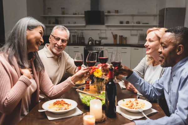 Amigos multiculturales sonrientes tintineando con copas de vino durante la cena - foto de stock
