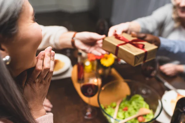 Cropped view of woman looking at her multicultural friends holding gift during dinner — Stock Photo