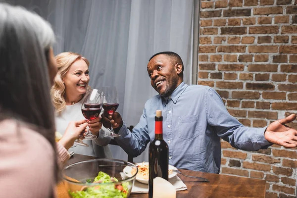 Recortado vista de la mujer tintineo con sonrientes amigos multiculturales durante la cena - foto de stock