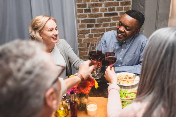 Cropped view of woman and man clinking with smiling multicultural friends during dinner — Stock Photo