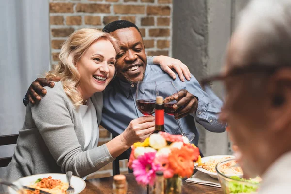 Focus selettivo di amici multiculturali sorridenti che si abbracciano e si accarezzano durante la cena — Foto stock