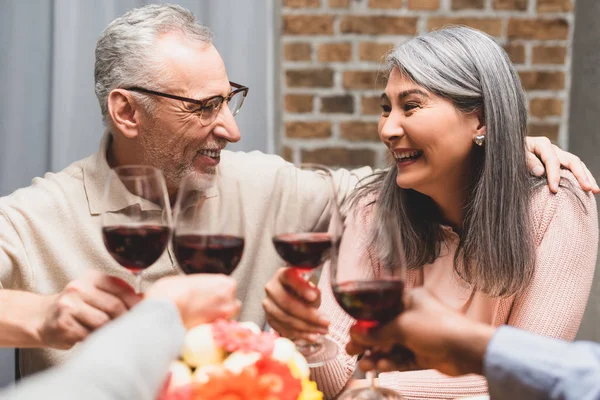 Cropped view of smiling multicultural friends hugging and clinking during dinner — Stock Photo