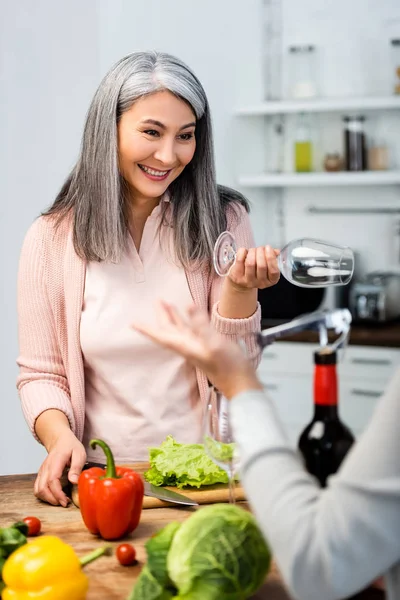 Selettivo fuoco di sorridere asiatico donna holding vino bicchiere e guardando il suo amico — Foto stock