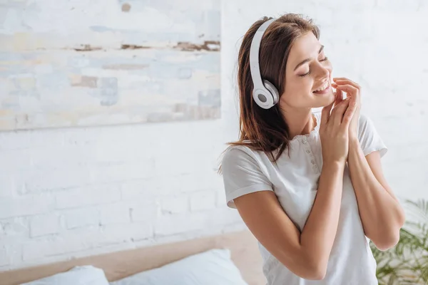 Mujer alegre con los ojos cerrados sonriendo y escuchando música en casa - foto de stock