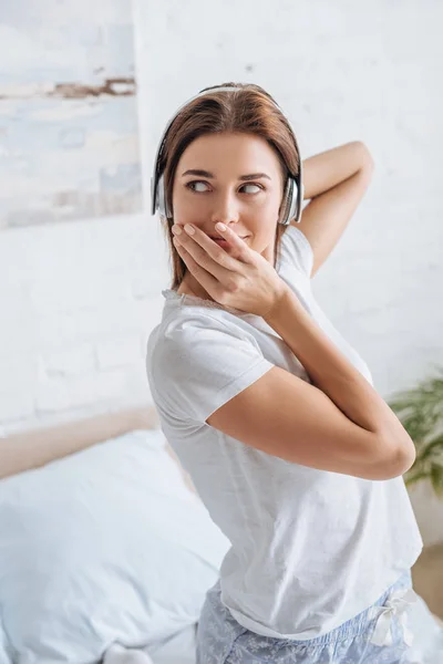 Jeune femme couvrant la bouche et écoutant de la musique à la maison — Photo de stock