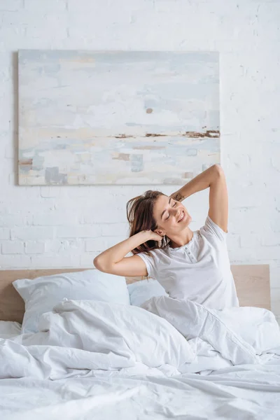 Chica soñadora sonriendo mientras toca el pelo en la cama - foto de stock
