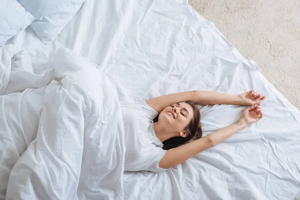 Top view of positive young woman with closed eyes resting in bed — Stock Photo