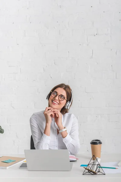 Femme d'affaires rêveuse écoutant de la musique dans les écouteurs tout en se relaxant au bureau — Photo de stock