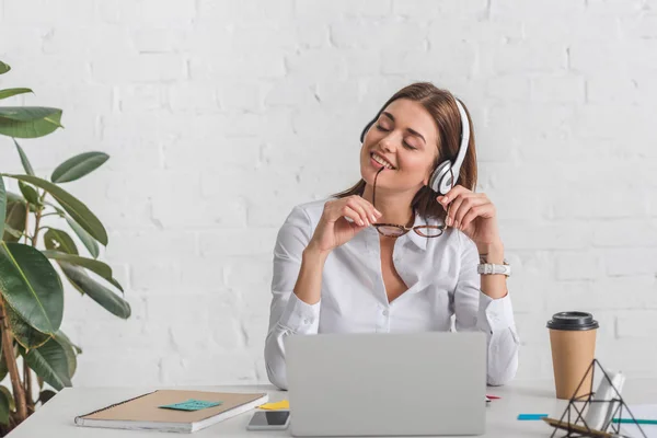Щаслива бізнес-леді слухає музику в навушниках, розслабляючись в офісі — стокове фото