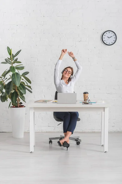 Alegre mujer de negocios escuchando música en auriculares mientras se relaja en la oficina - foto de stock