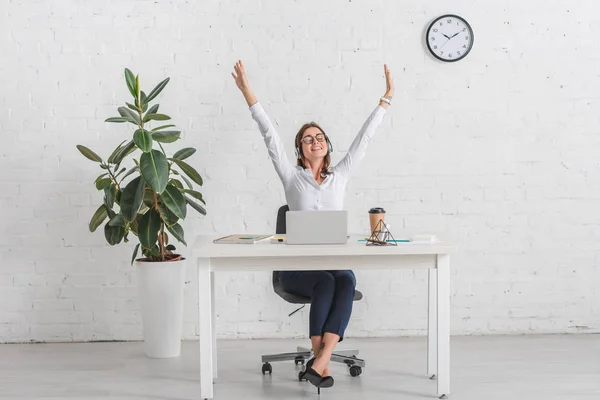 Позитивная деловая женщина слушает музыку в наушниках во время отдыха в офисе — стоковое фото