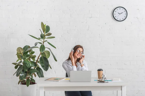 Jeune femme d'affaires heureuse écouter de la musique dans les écouteurs tout en se relaxant au bureau — Photo de stock