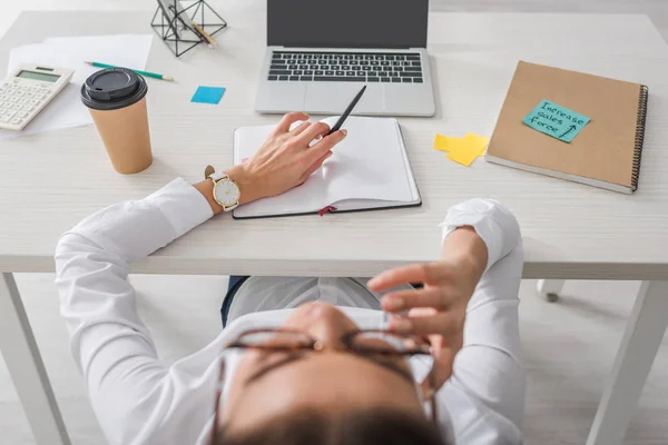 Foco selectivo de la computadora portátil en la mesa cerca de la mujer de negocios descansando en la oficina - foto de stock