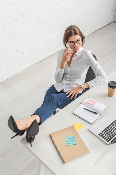 Vista aerea di allegra donna d'affari che si rilassa e parla sullo smartphone in ufficio — Foto stock