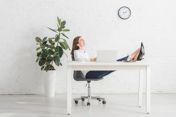 Мечтательная деловая женщина отдыхает рядом с ноутбуком в офисе — стоковое фото