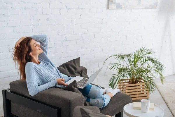 Vue latérale de femme heureuse refroidissant avec ordinateur portable à la maison — Photo de stock