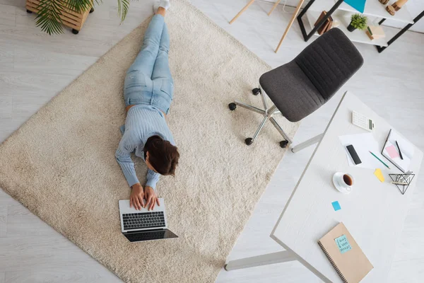 Blick auf Bloggerin, die auf Teppich liegt und Laptop benutzt — Stockfoto