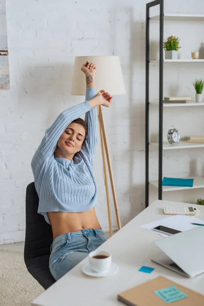 Attractive young woman dreaming while stretching near gadgets on table — Stock Photo