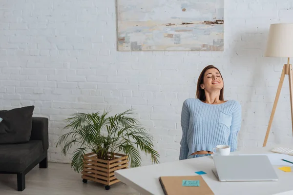 Joven mujer de ensueño sonriendo cerca de la mesa en casa - foto de stock