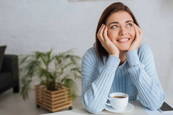 Jovem mulher sonhadora sorrindo perto da xícara com café — Fotografia de Stock