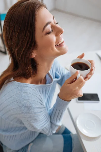 Веселая молодая женщина улыбается, держа чашку кофе — стоковое фото