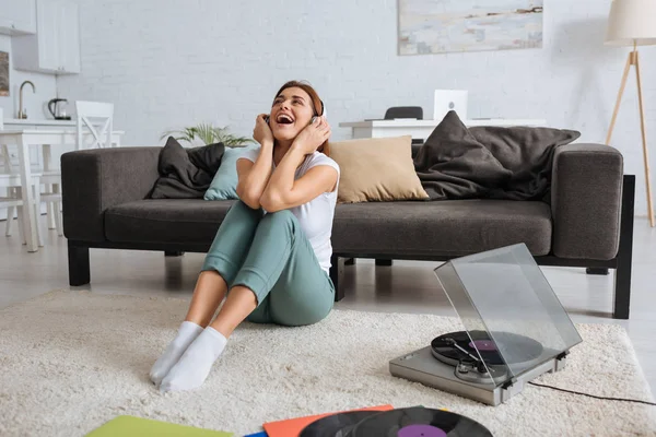 Alegre chica escuchando música en auriculares y cantando cerca de vintage tocadiscos - foto de stock