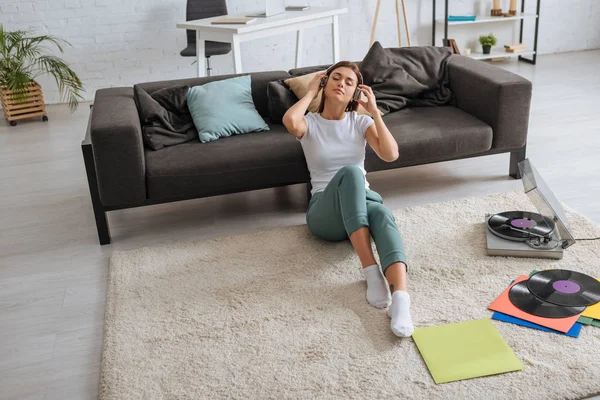 Dreamy girl listening music in headphones near sofa and vintage record player — Stock Photo