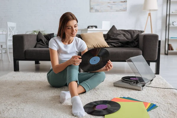 Fille souriante tenant un record de vinyle tout en refroidissant à la maison — Photo de stock