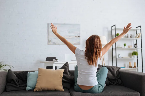 Back view of girl with outstretched hands sitting on sofa — Stock Photo