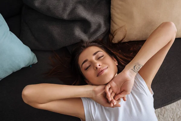 Вид сверху на счастливую татуированную девушку с закрытыми глазами, охлаждающуюся на диване — стоковое фото