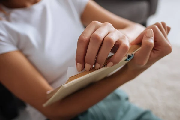 Vista ritagliata di giovane donna che tiene libro mentre si agghiaccia a casa — Foto stock
