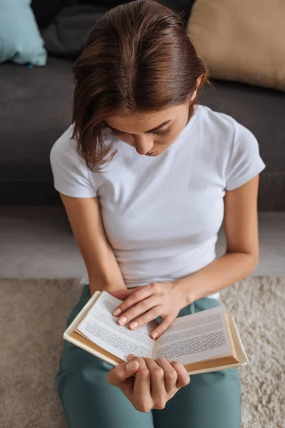 Vue aérienne du livre de lecture femme assis sur le tapis près du canapé — Photo de stock