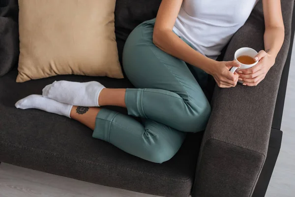 Vista ritagliata della donna raffreddamento del divano con tazza di tè — Foto stock