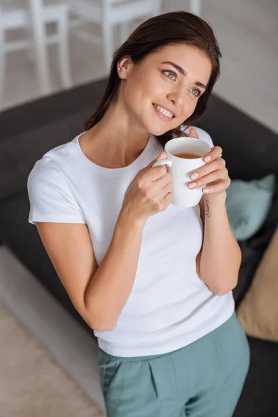 Mulher atraente sonhando e segurando xícara de chá — Fotografia de Stock